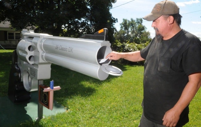 In this photo taken Thursday, Sept. 5, 2013, Roger Buchko grabs mail from his mailbox that resembles a giant Smith & Wesson .44 magnum revolver in Lopatcong Township, N,J. Mail is placed in a small compartment at the mouth of the gigantic gun barrel. (AP Photo/The Express-Times, Sue Beyer)